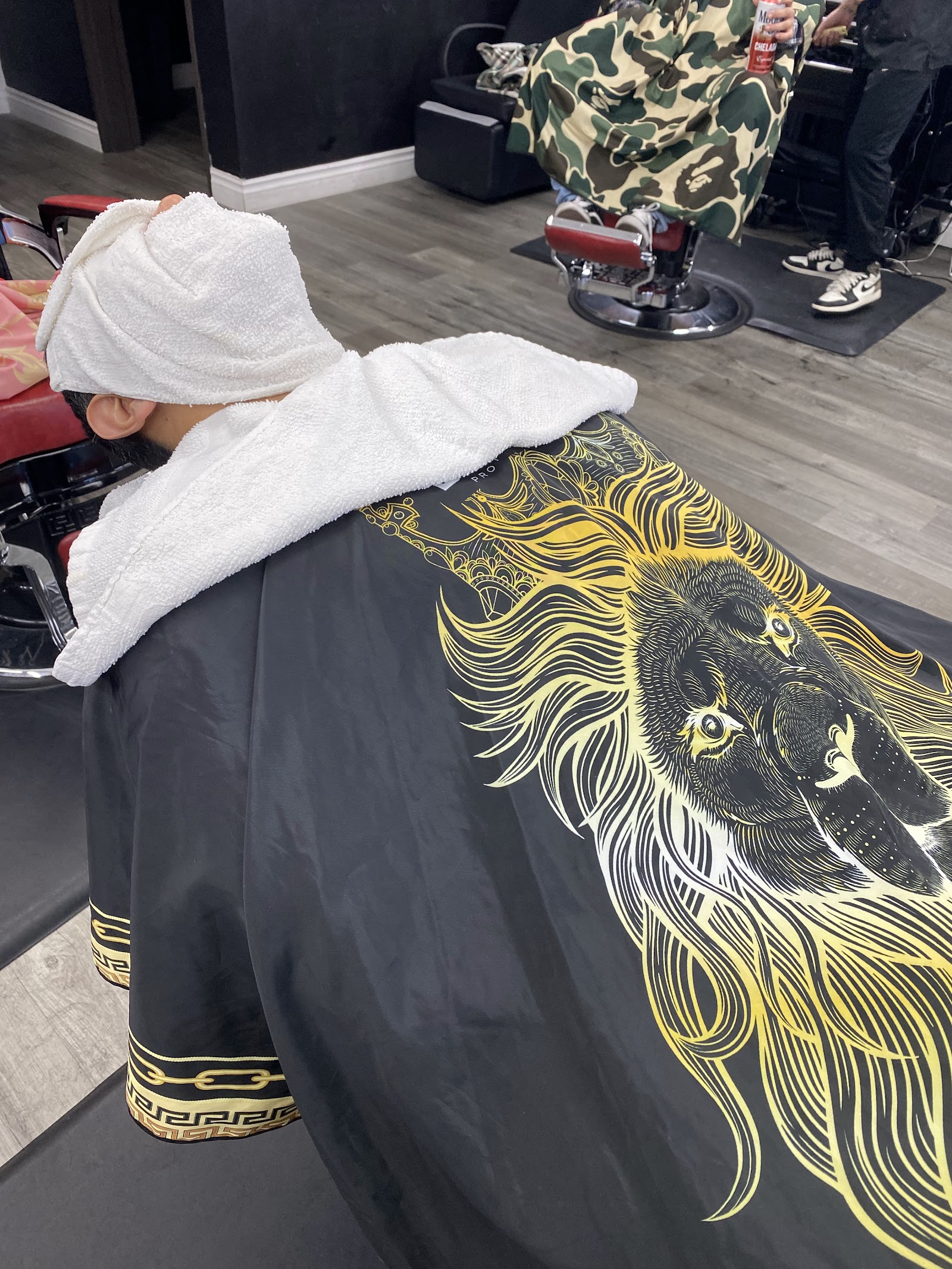 Client reclined with a hot towel and lion-print cape during a barbershop service
