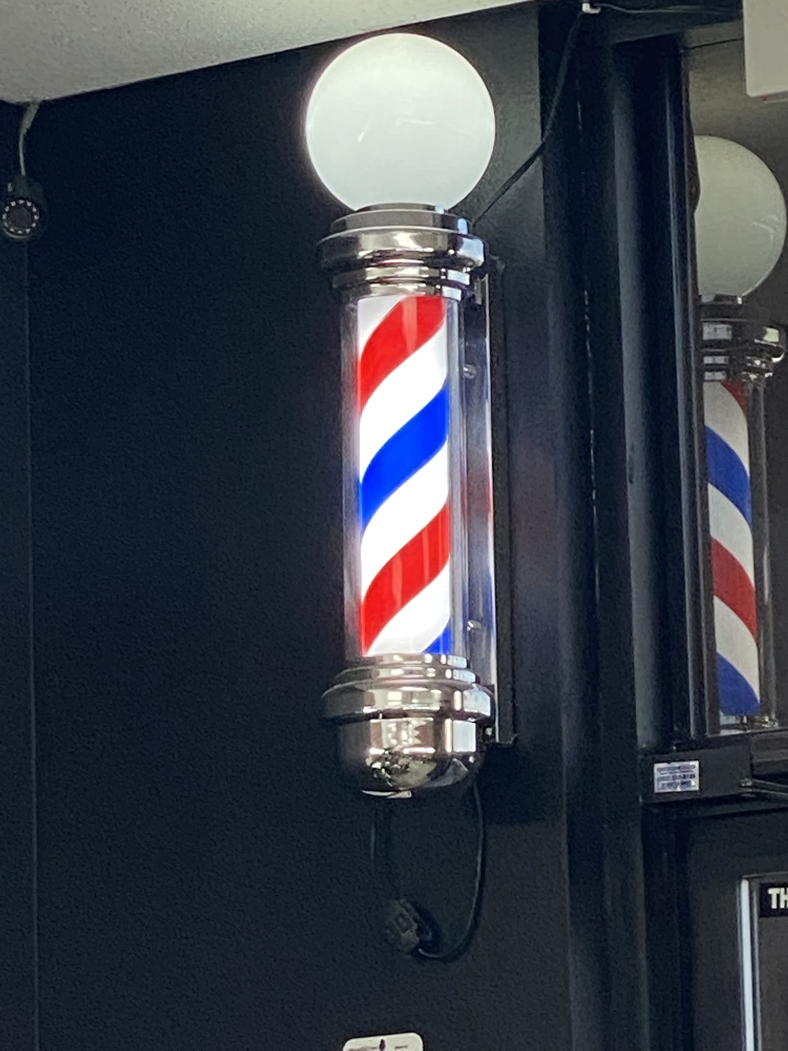 Illuminated barber pole mounted on a dark wall inside the shop
