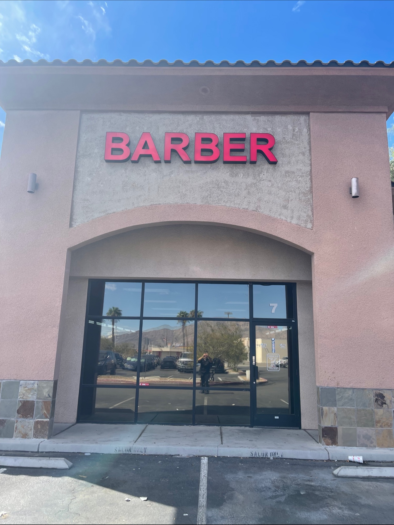Exterior of Mr. G’s Classic Barbershop with a large red BARBER sign under a blue sky